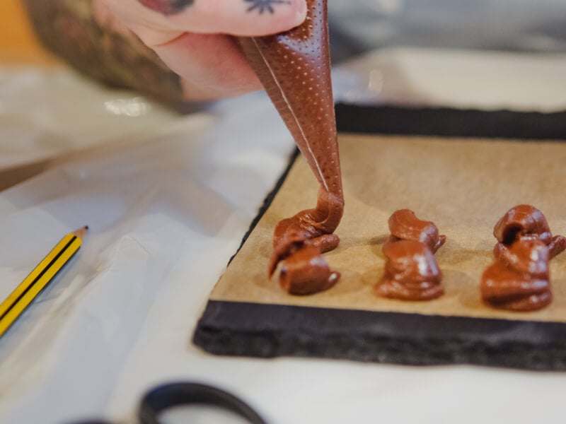 A person piping chocolate truffles onto a lined tray